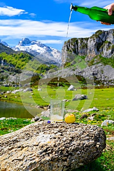 Pouring from green bottle and high height of natural Asturian cider made fromÂ fermented apples with view on Covadonga lake and